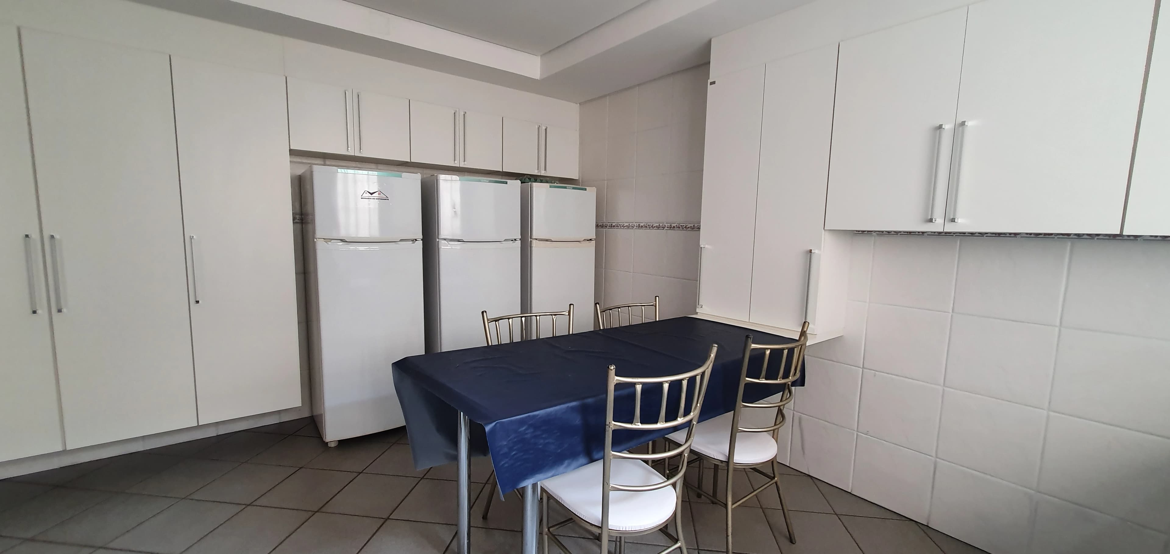 Cozinha com armários brancos, geladeiras e mesa de refeições