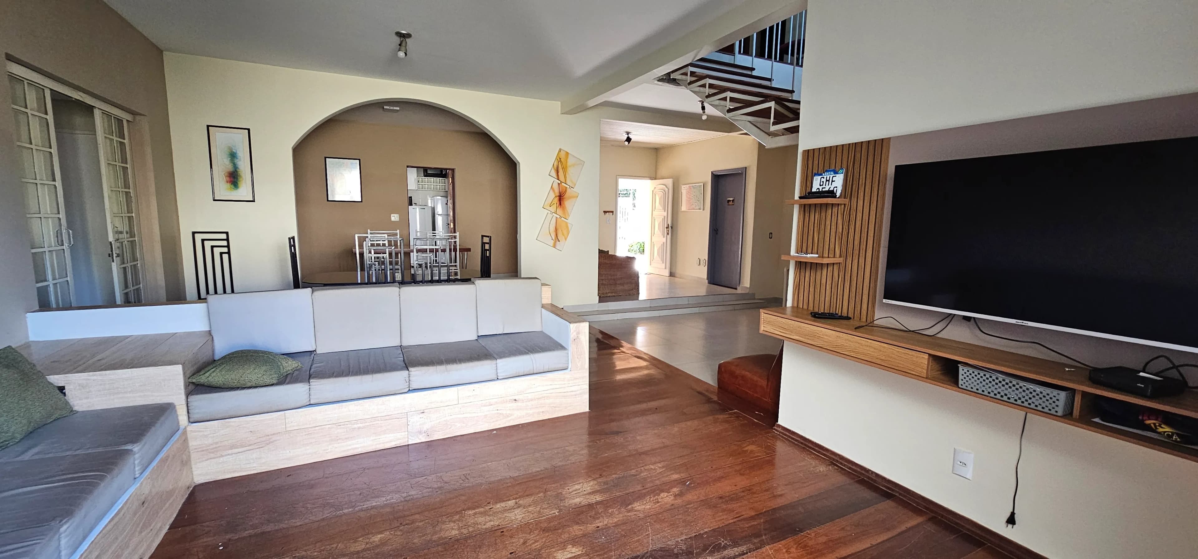 Sala com sofá cinza, televisão e piso de madeira